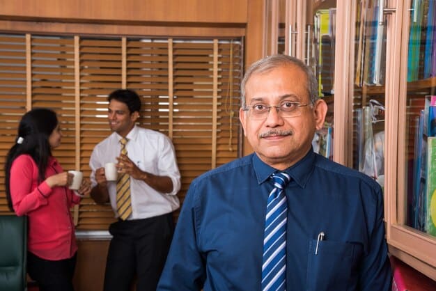 A still photo of Shiv Roy in a sophisticated pantsuit, standing in a campaign office. She's talking intently to a campaign manager, with posters and political paraphernalia visible in the background.