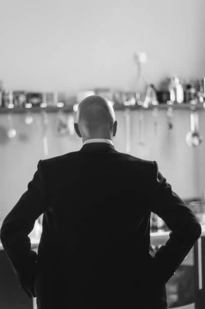 A close-up, slightly blurred, candid black-and-white photograph of a director, framed from the shoulders up, looking intently at a monitor on set. The director is young and surrounded by equipment, subtly indicating this is an indie film production. The natural light and handheld-style composition emphasize the intimate and gritty nature of independent filmmaking.