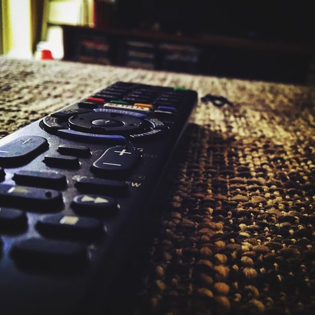 A close-up of several remote controls on a couch, each with a different streaming service icon displayed on the TV screen, representing the current fragmented streaming landscape.