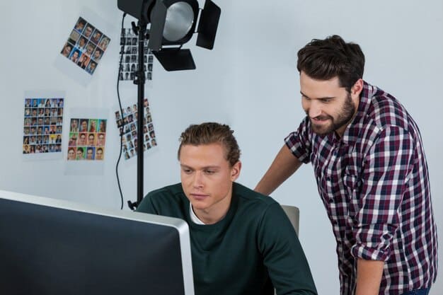 Two film editors engaged in a lively discussion in front of a large screen displaying a scene. One is gesturing emphatically while the other is listening attentively, with scripts and notes scattered around them.